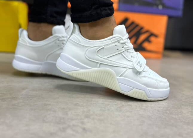 White sneakers worn by a person on a neutral background with Nike boxes in the background.